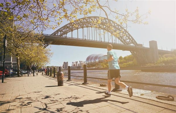 Man running along riverside underneath a bridge